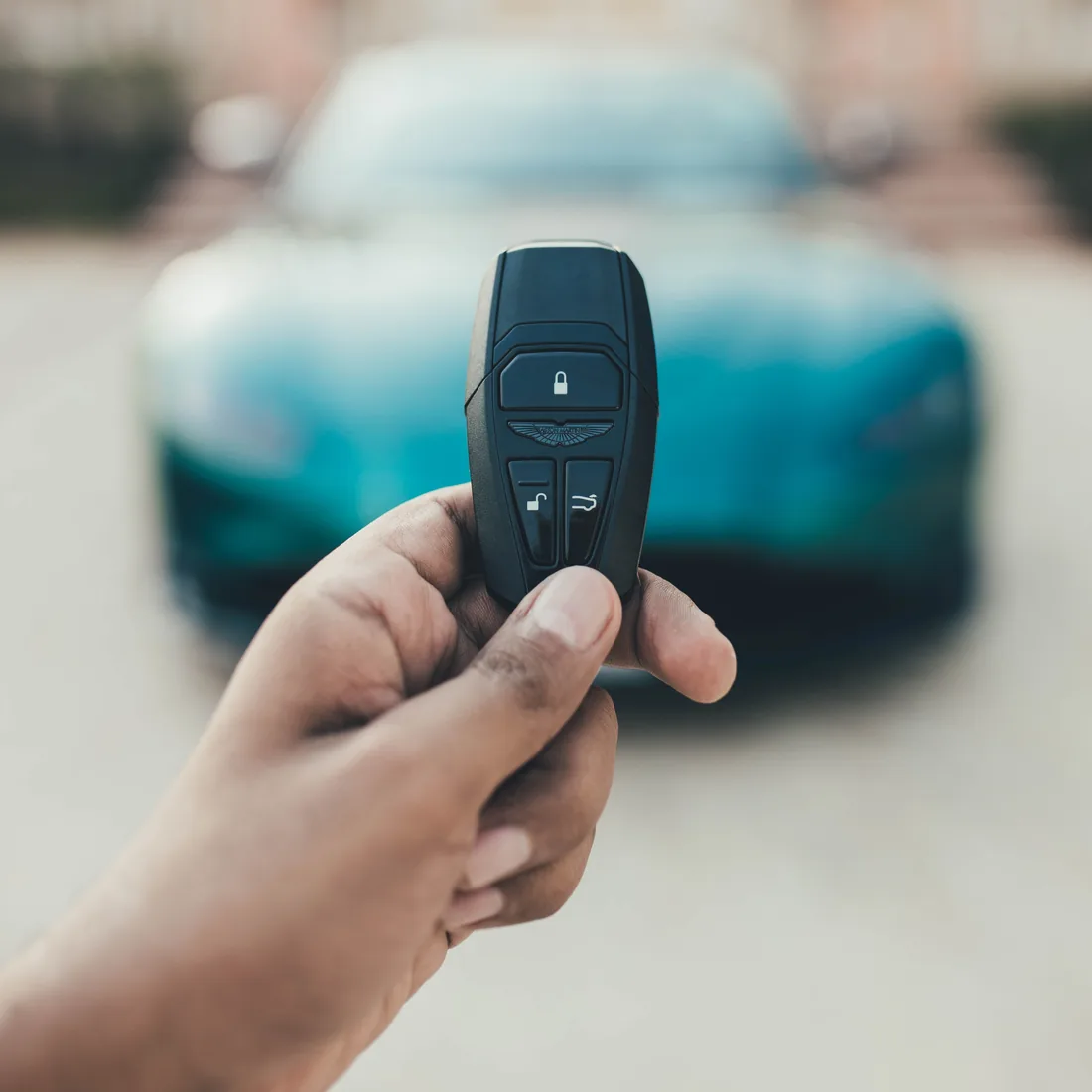 Hand holding a car remote key fob in front of a vehicle