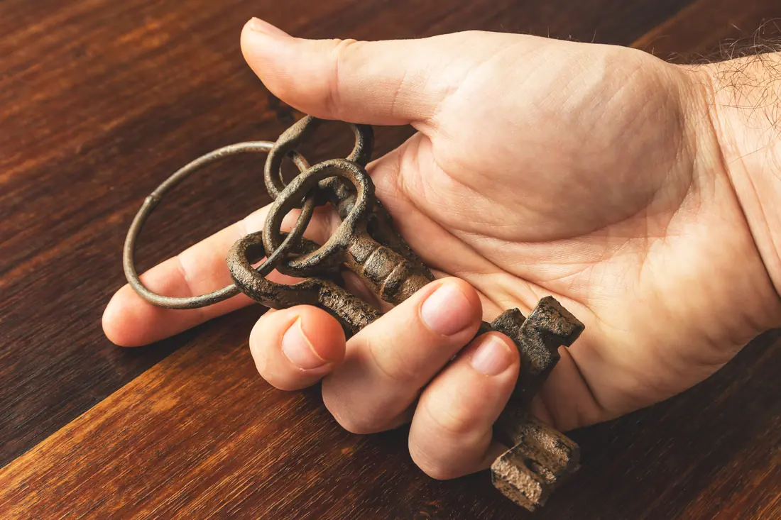 Handful of old keys held over a wooden surface